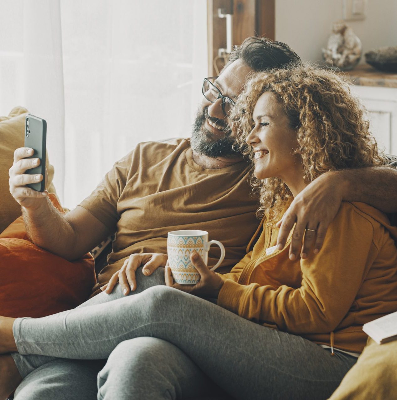 Smiling couple relax on a sofa taking a selfie while the woman holds a mug